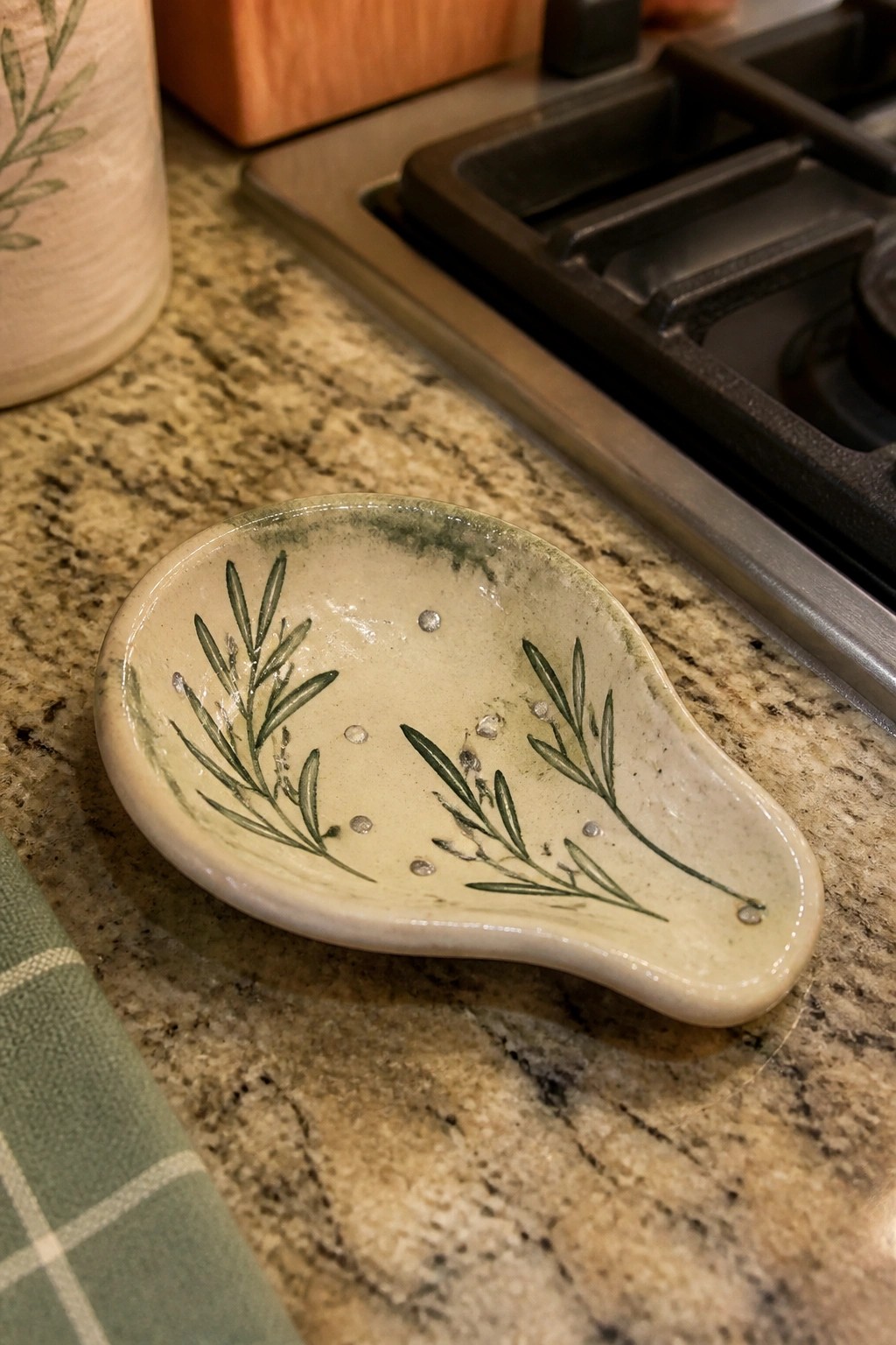Cream-colored ceramic spoon rest with green herb design on granite counter