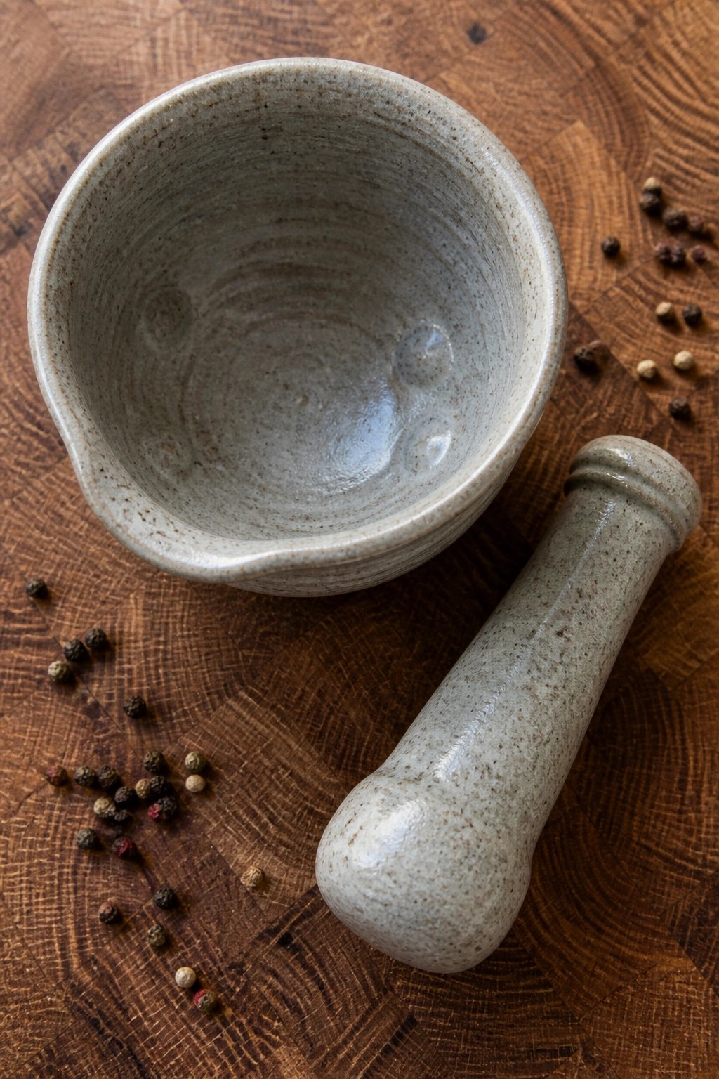 Ceramic mortar and pestle beside scattered peppercorns on wooden cutting board