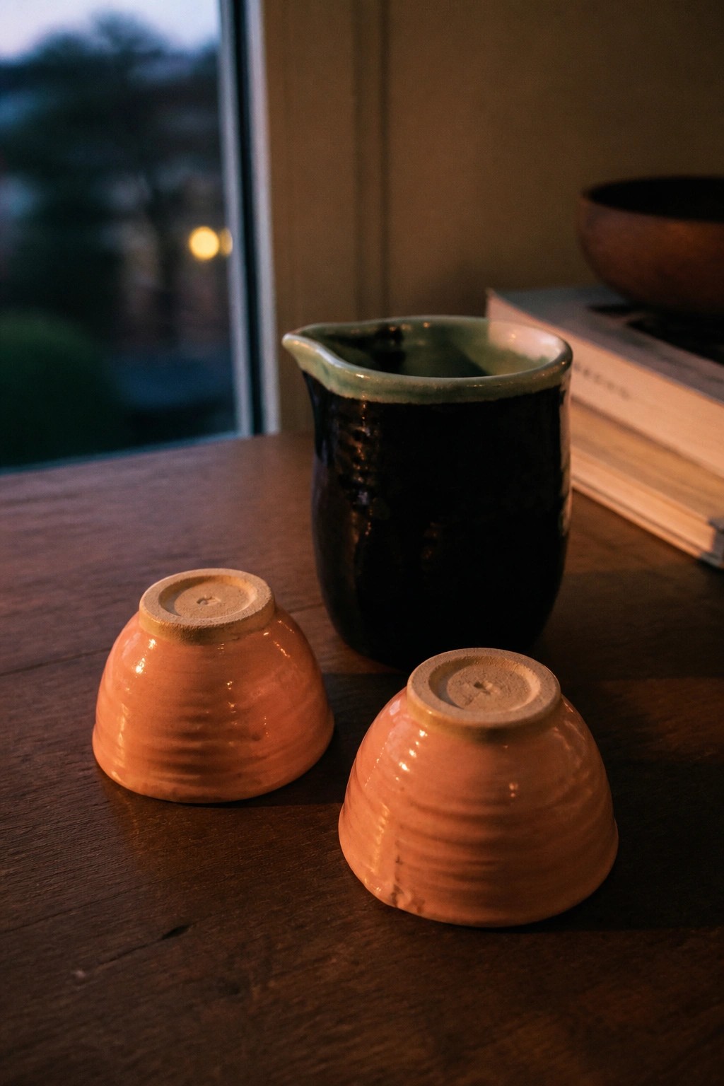 Two upside-down orange ceramic bowls beside a dark green pitcher on wooden table