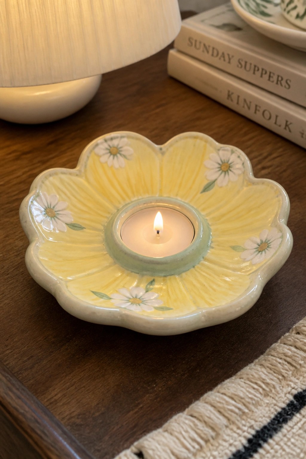 Yellow flower-shaped ceramic holder with lit tealight on wooden table beside books