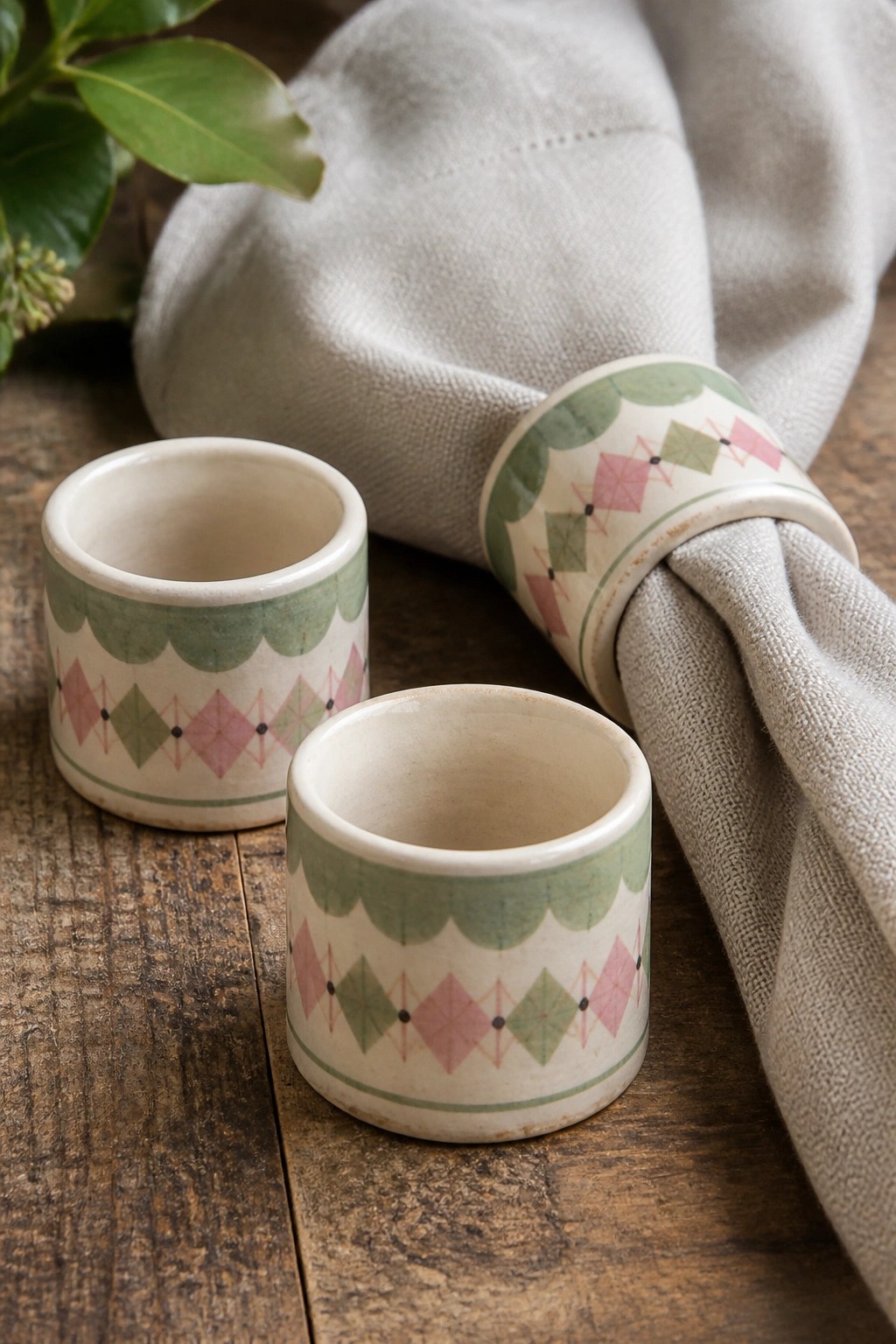 Two ceramic napkin rings with pink-green diamonds, one holding gray linen on wood.