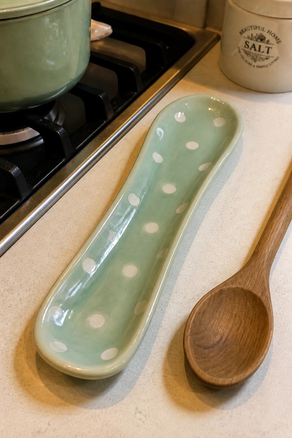 Green polka-dotted ceramic dish beside wooden spoon on kitchen counter.