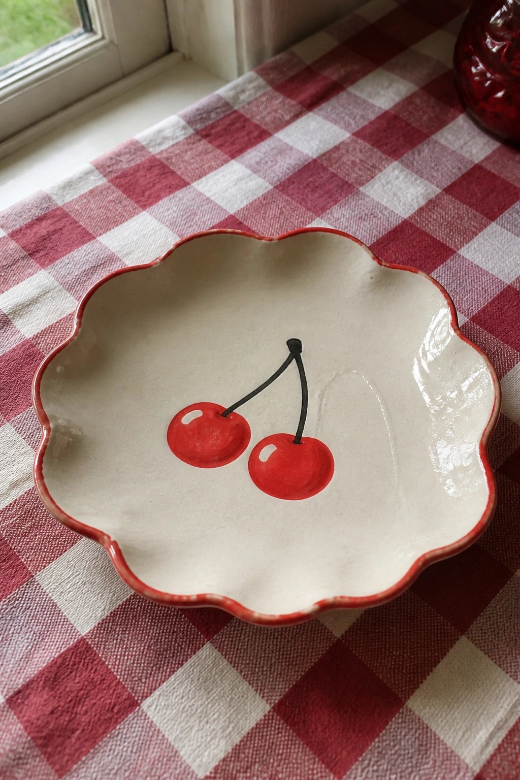 Scalloped ceramic bowl with red cherries on red and white checkered tablecloth