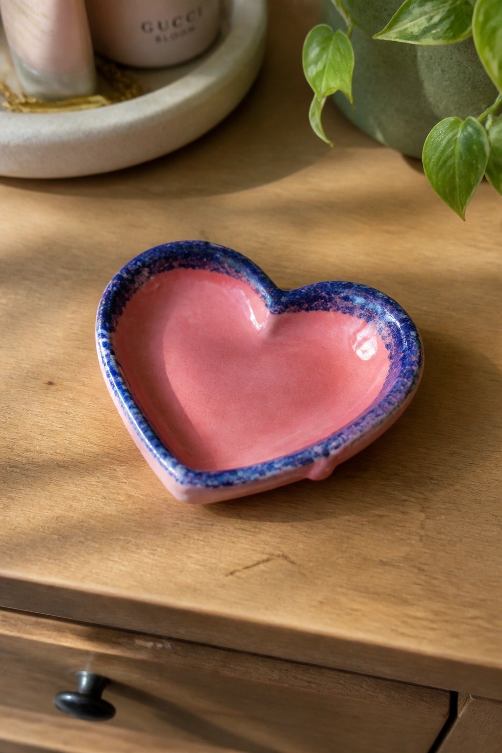 Pink heart-shaped ceramic bowl with blue speckled rim on wooden table