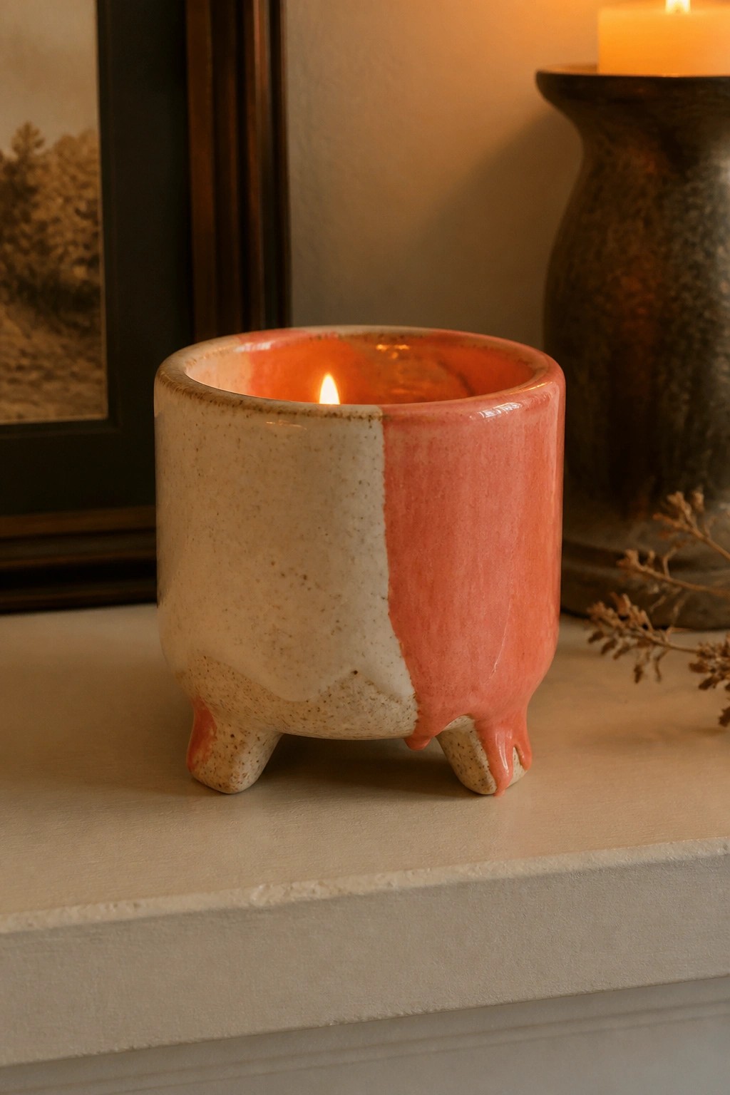 Two-toned pink and beige ceramic pot with dripping glaze holding lit candle.