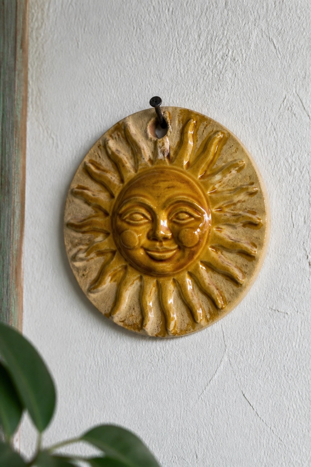 Yellow ceramic sun face with rays hanging on white wall by nail