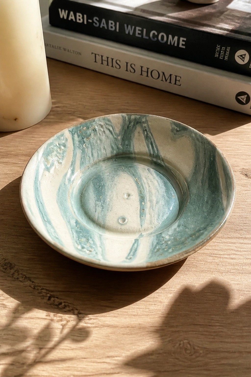 Marbled teal ceramic bowl on wooden table beside stacked books and candle.