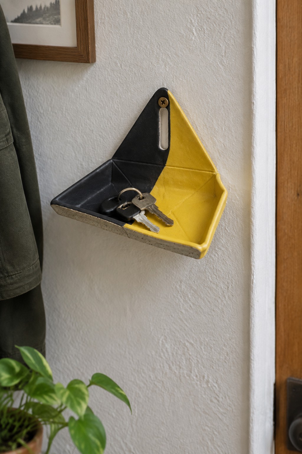 Yellow and black ceramic key tray with keys on white wall beside plant