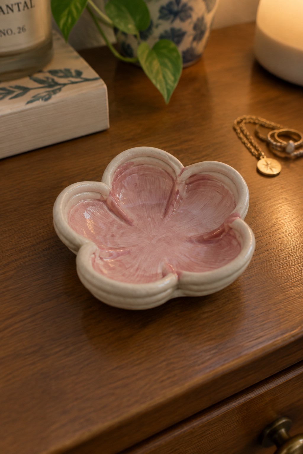 Pink flower-shaped ceramic bowl on wooden table with gold jewelry nearby