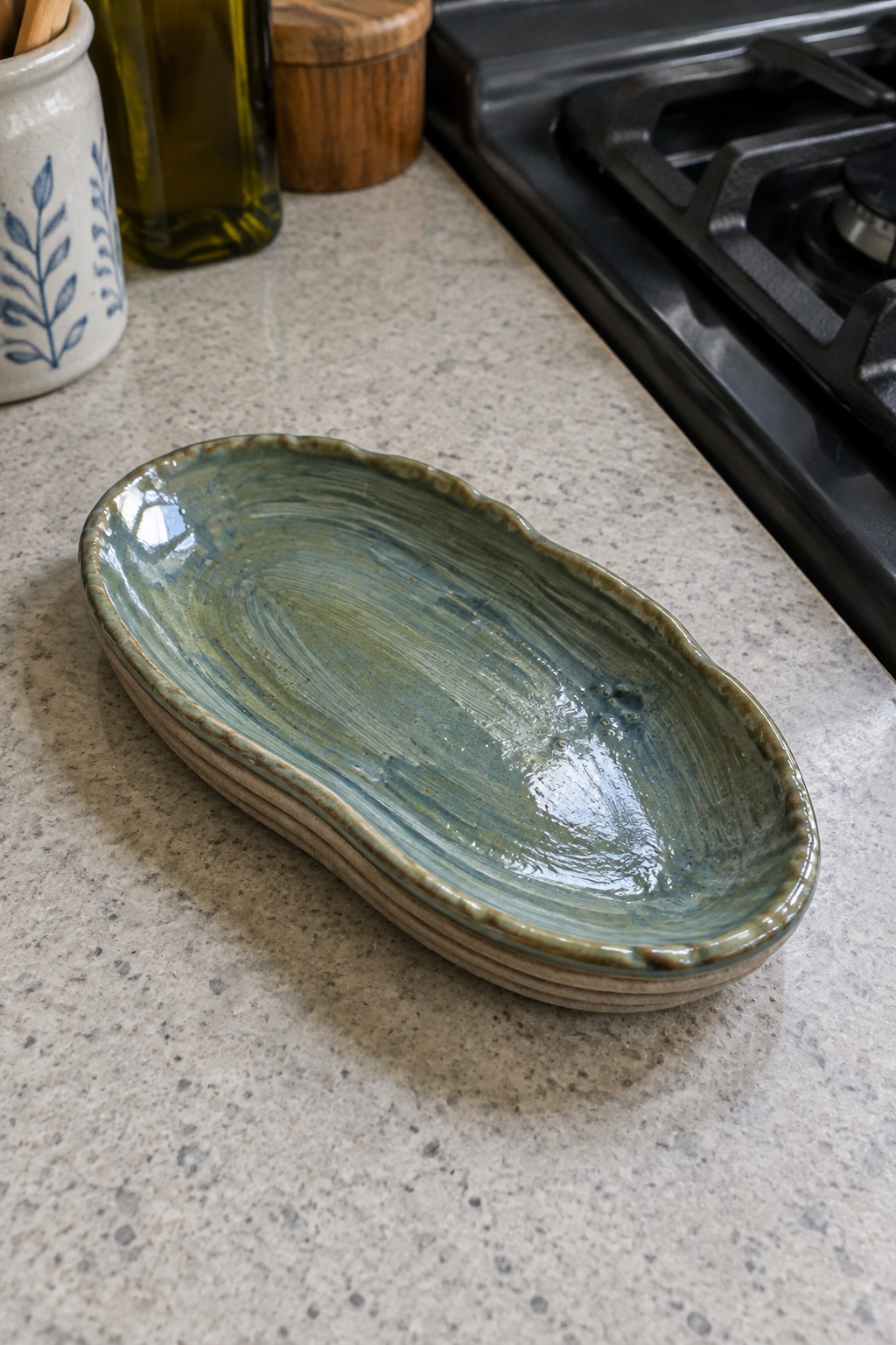 Stacked blue-green glazed ceramic oval dishes on kitchen countertop by stove