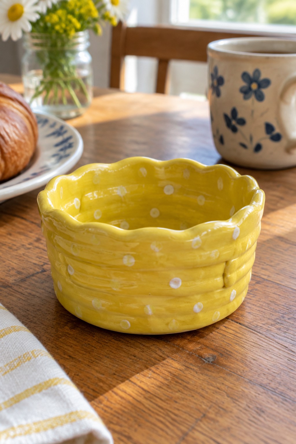 Yellow polka-dot bowl on wooden table with floral mug, croissant, and flowers