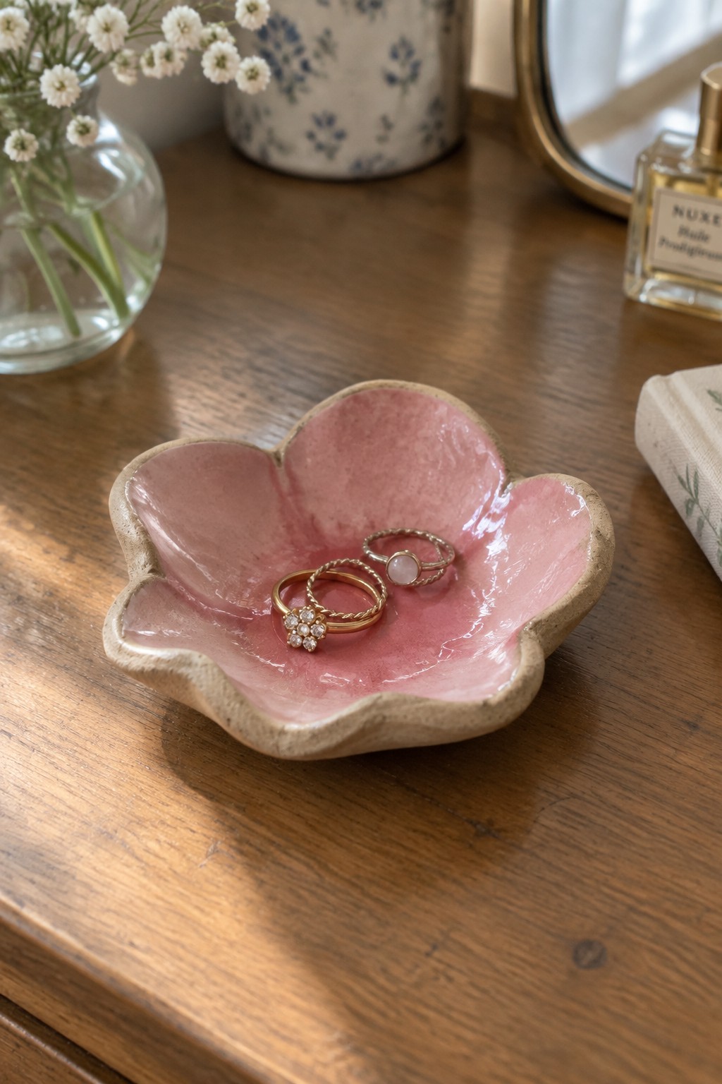 Pink flower-shaped ceramic dish holding gold rings on wooden vanity table