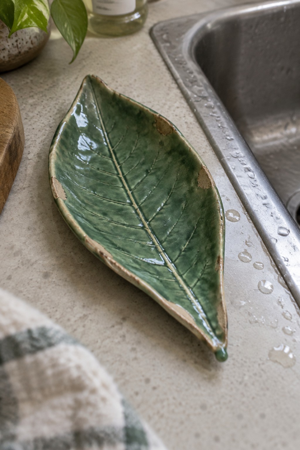 Green ceramic leaf-shaped dish on wet countertop beside stainless steel sink