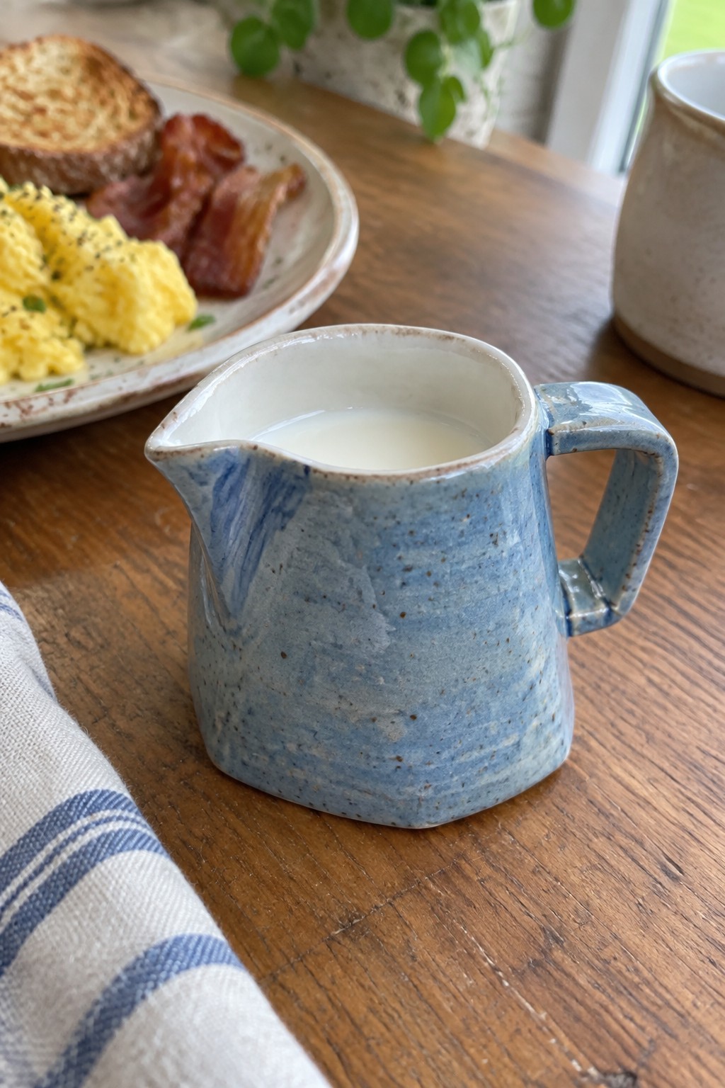 Blue ceramic pitcher of milk on wooden table beside breakfast plate