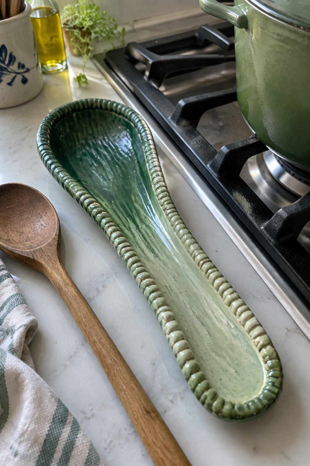 Green ceramic spoon rest beside wooden spoon on marble kitchen counter
