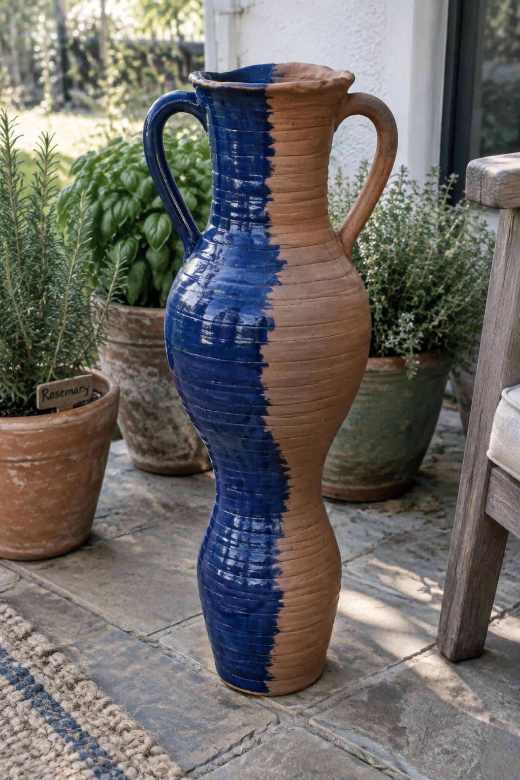 Tall two-handled ceramic vase half blue-glazed half terracotta on stone patio