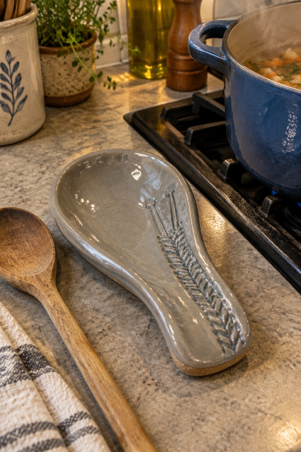 Gray ceramic spoon rest with wheat design beside wooden spoon on marble counter