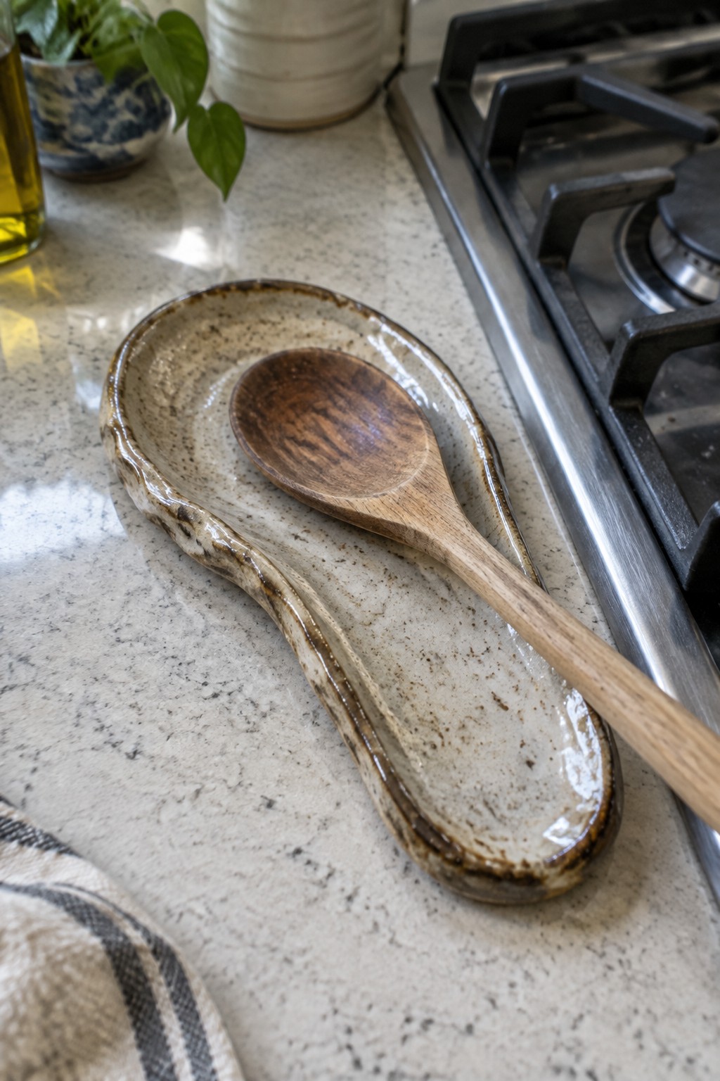 Wooden spoon on speckled ceramic rest beside gas stove on kitchen counter