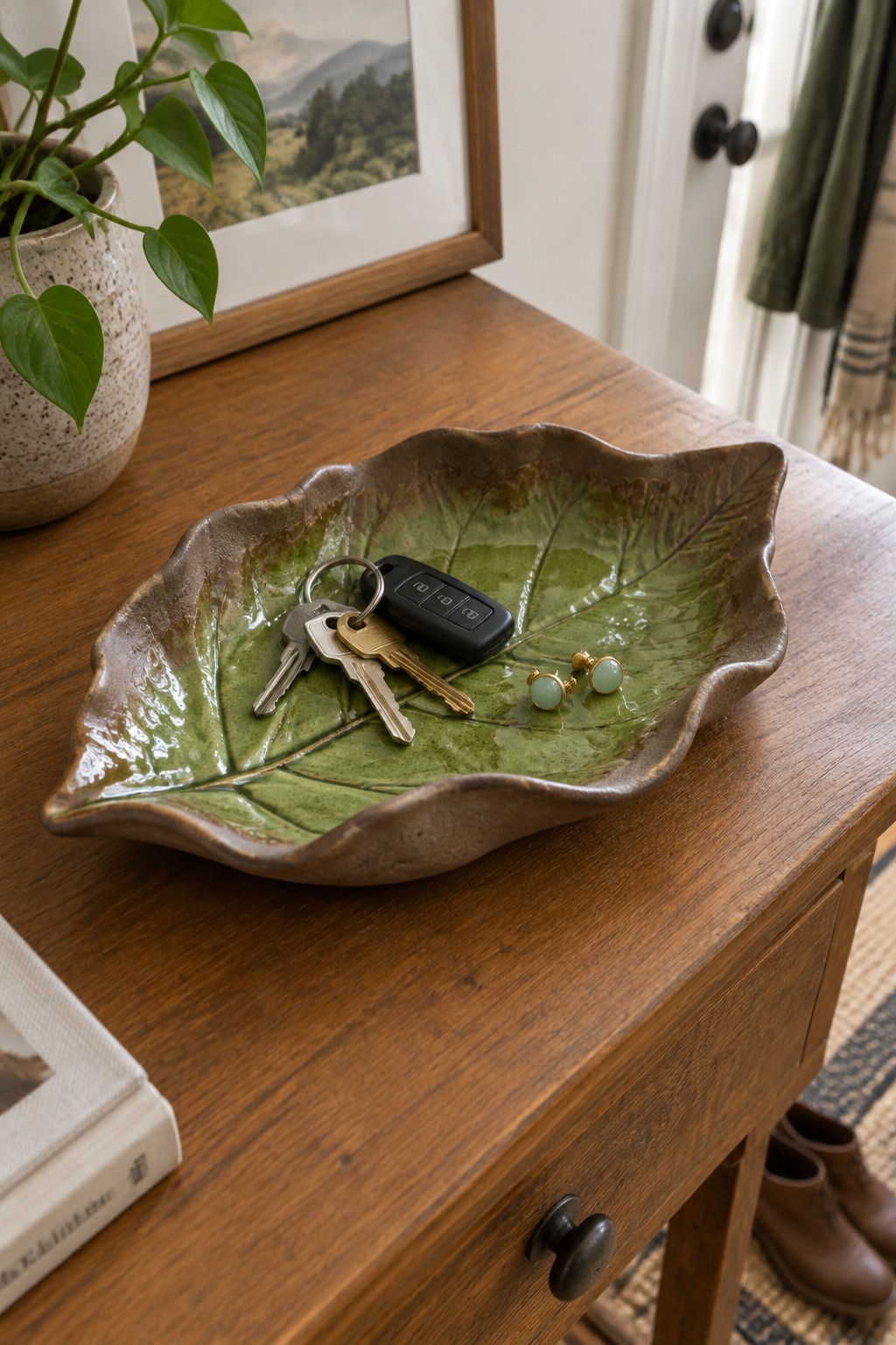 Green leaf-shaped ceramic bowl holding keys and earrings on wooden table