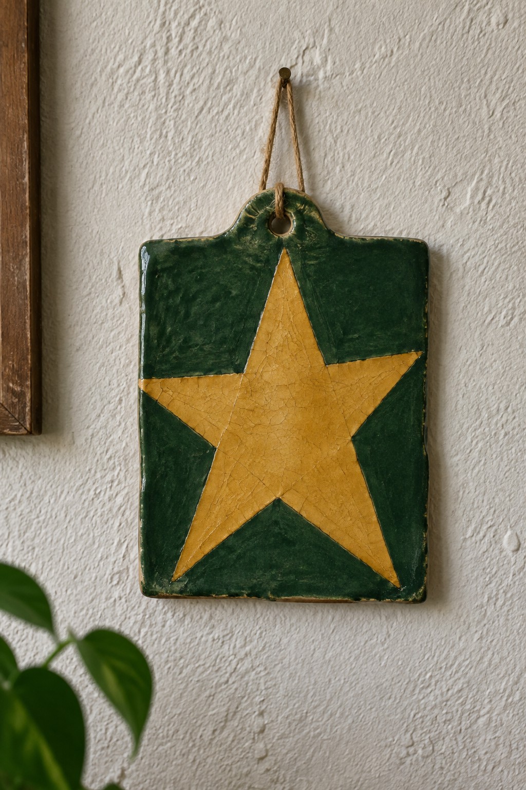 Green ceramic tile with yellow star hanging on white wall by twine