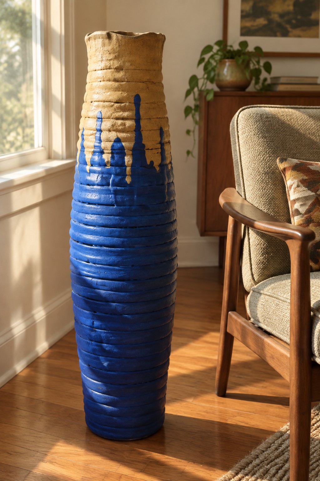 Tall blue and beige ceramic vase with dripping glaze beside wooden armchair