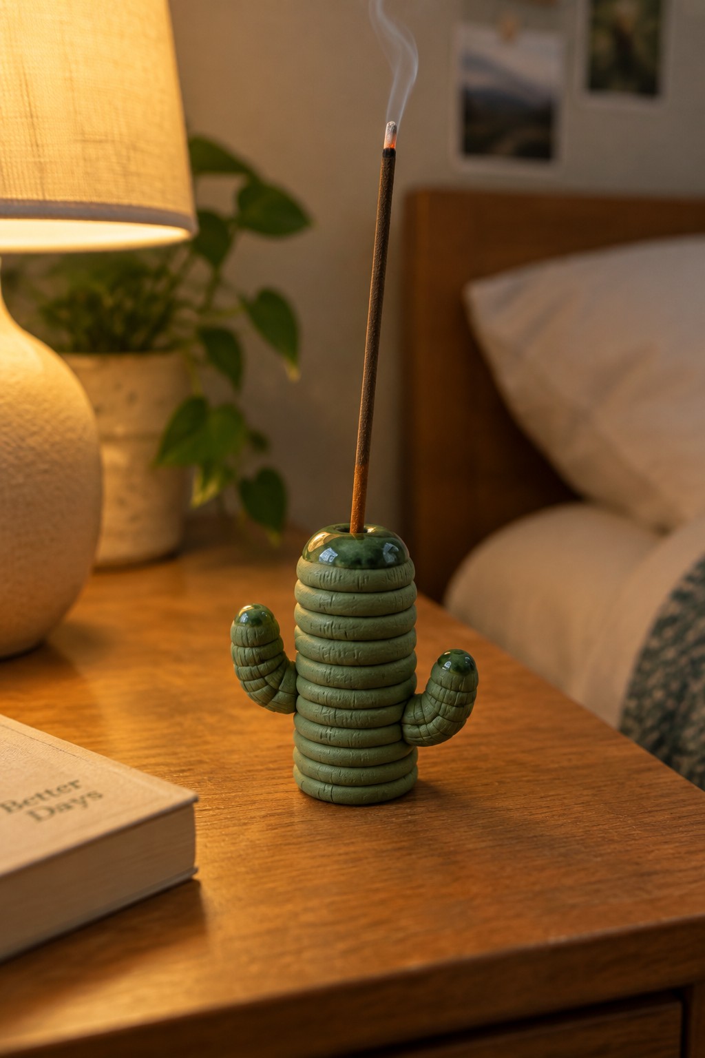 Green cactus incense holder with lit smoking stick on wooden bedside table
