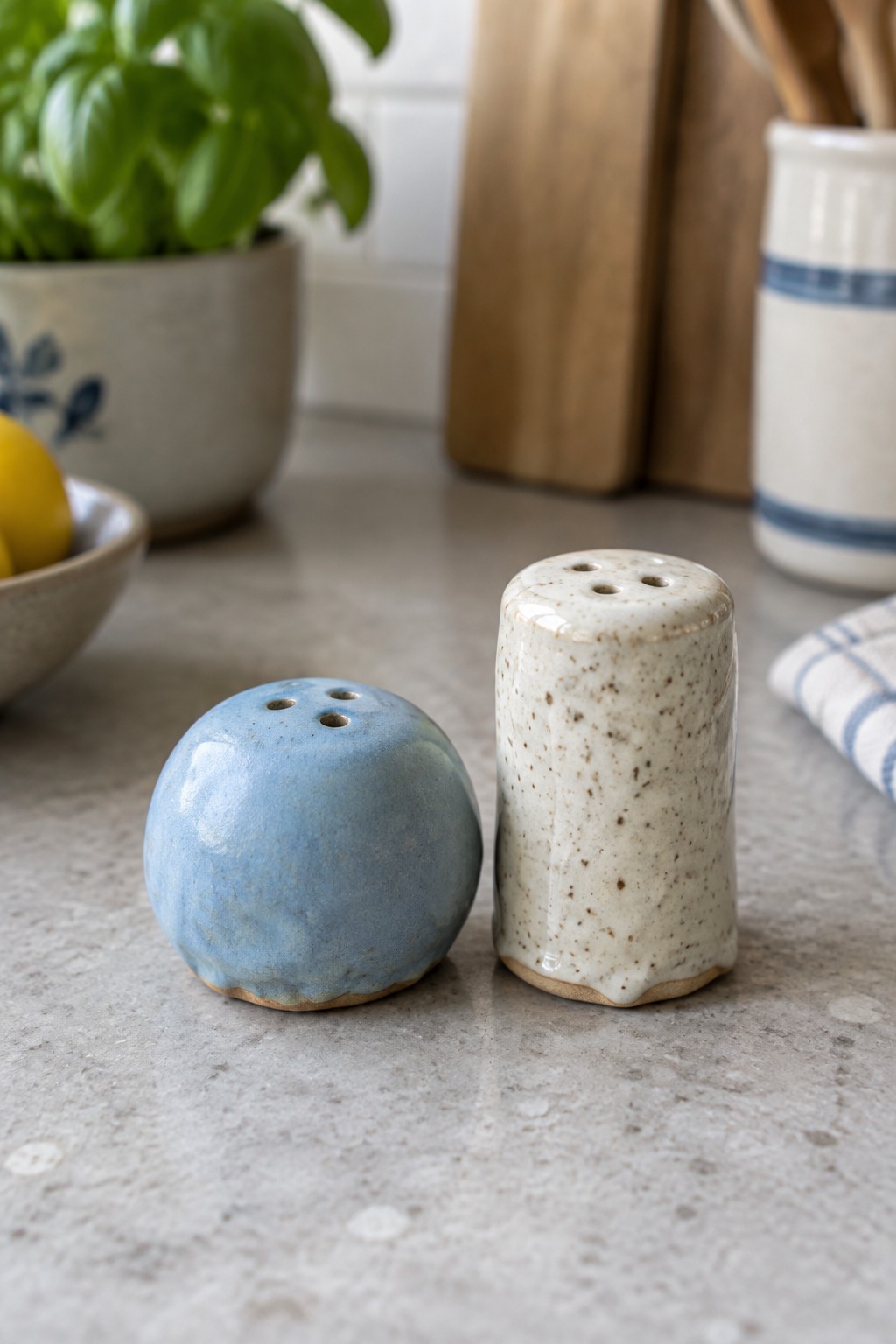 Blue and speckled white ceramic shakers on gray kitchen countertop with basil plant