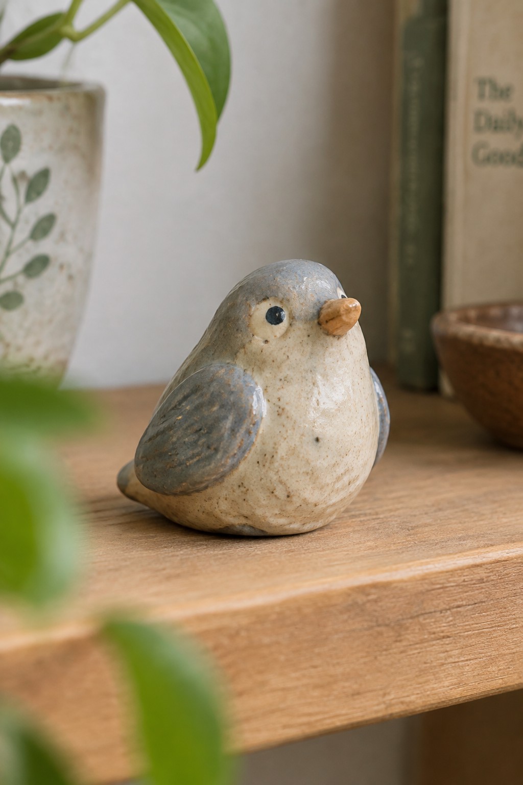 Small ceramic bird in beige and gray with brown beak on wooden table.