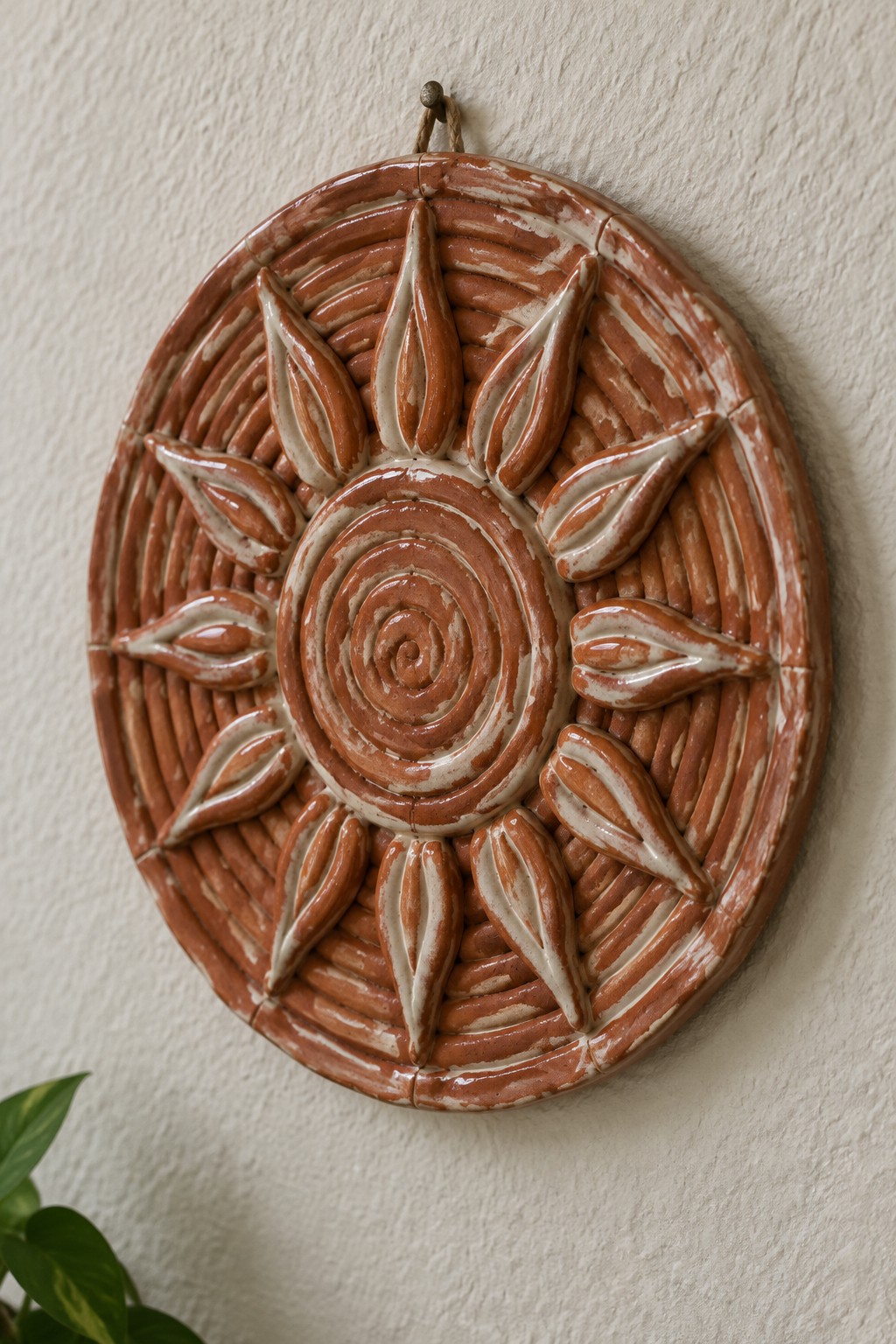 Terracotta ceramic sun with spiral center and white-glazed rays on wall