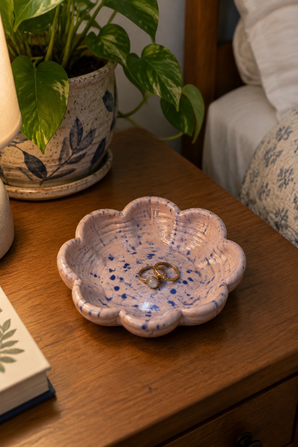 Pink speckled scalloped dish with gold rings on wooden nightstand near plant