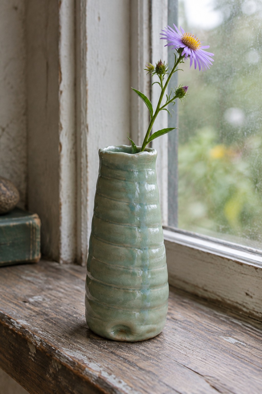 Green ribbed ceramic vase with purple aster on wooden windowsill