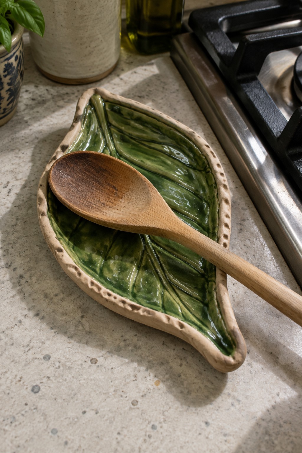 Green ceramic leaf dish holding wooden spoon on kitchen countertop