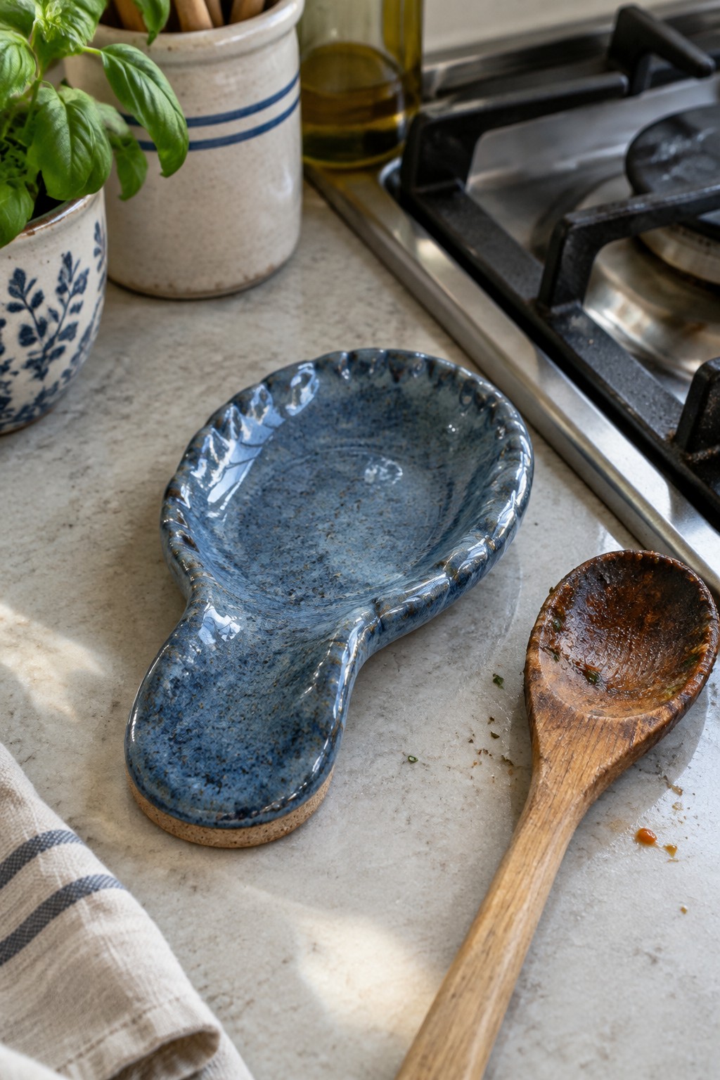 Blue ceramic spoon rest beside wooden spoon on marble kitchen counter with basil