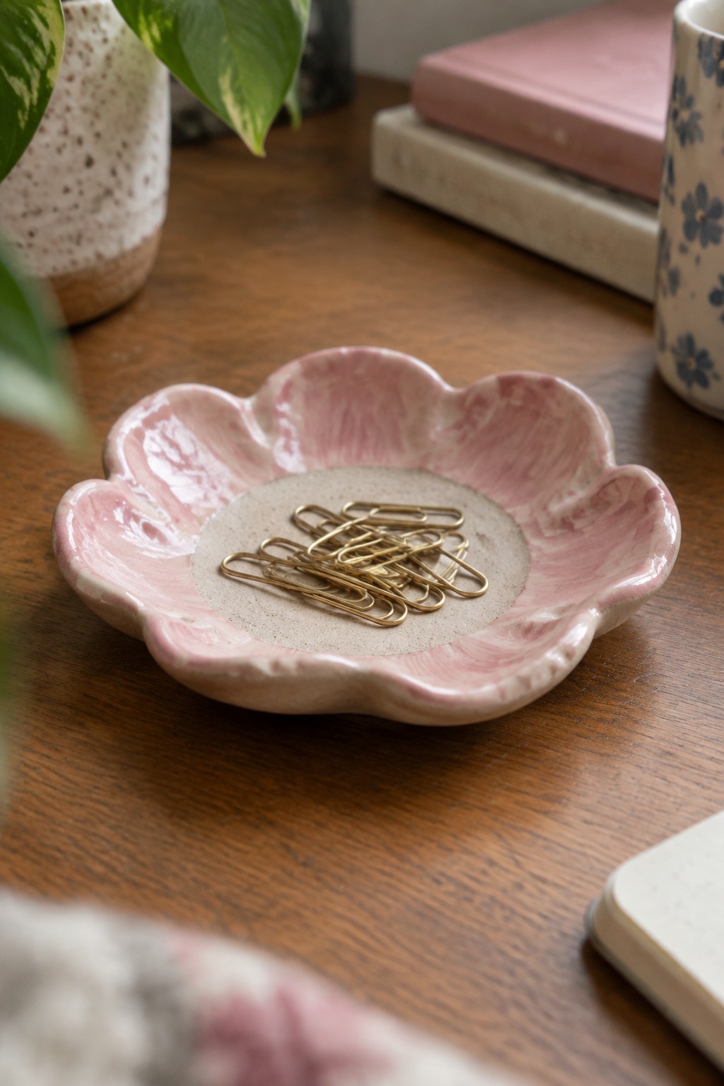 Pink marbled flower-shaped ceramic dish with gold paper clips on wood table