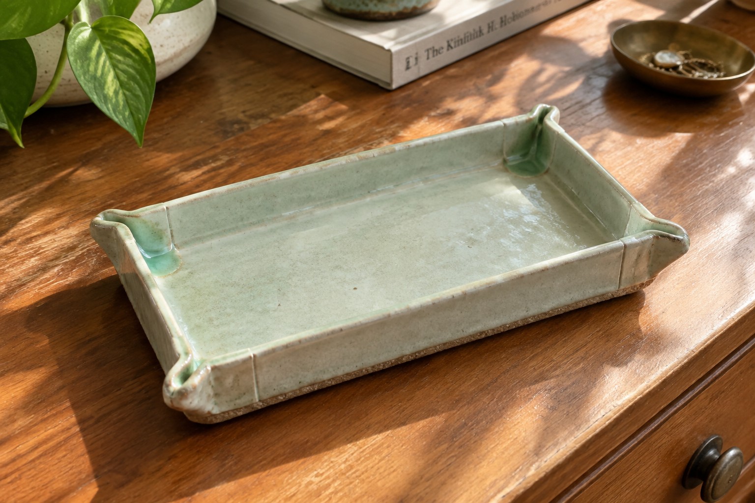 Mint green ceramic tray with gold necklace, rings and hoops on wood table.