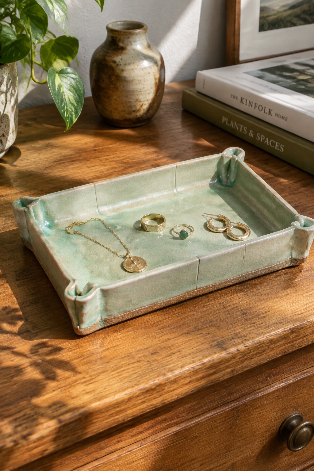 Mint green ceramic tray with gold necklace, rings and hoops on wood table.