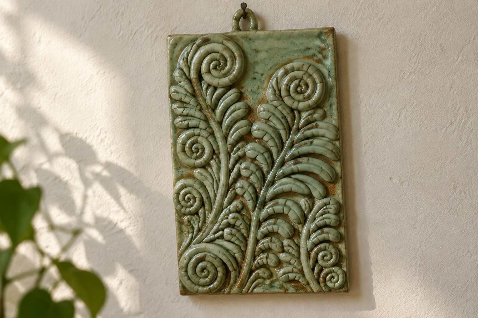 Green ceramic plaque with raised spirals and leaf patterns on sunlit wall