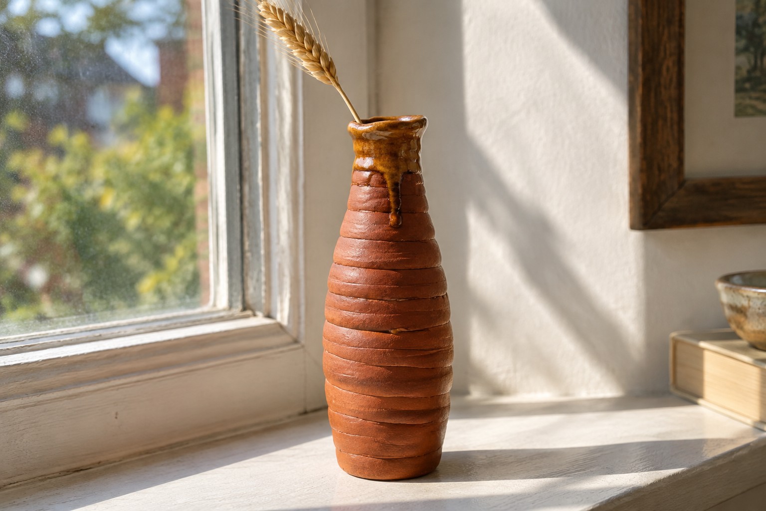Brown ribbed ceramic vase with dripping glaze holding wheat stalk on windowsill