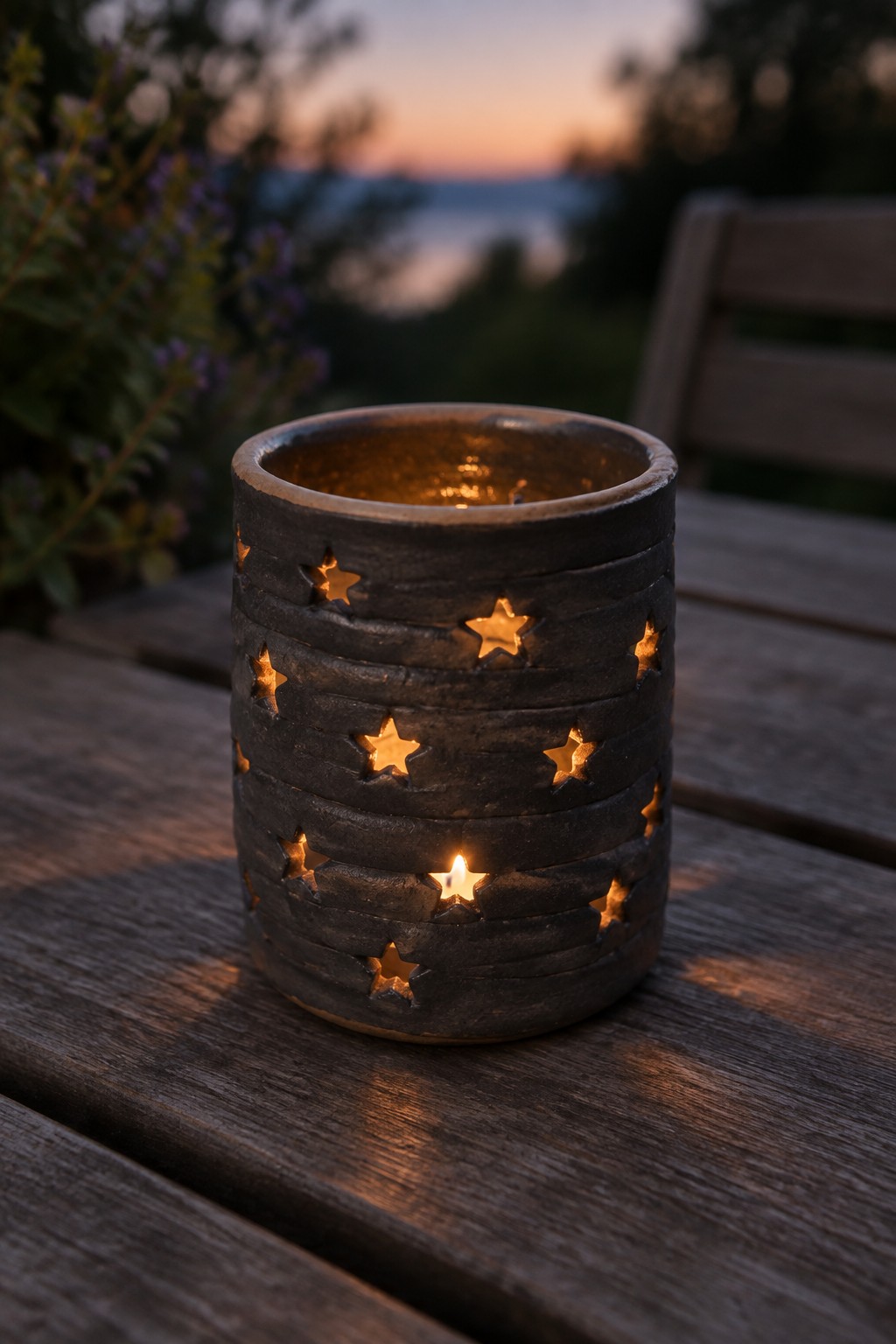 Lit star-cutout candle holder glowing on wooden table at outdoor dusk