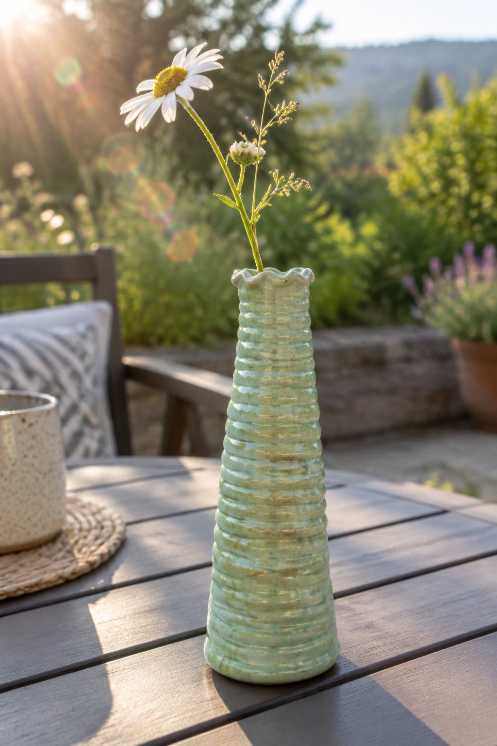 Light green ribbed ceramic vase with white daisy on sunny wooden table
