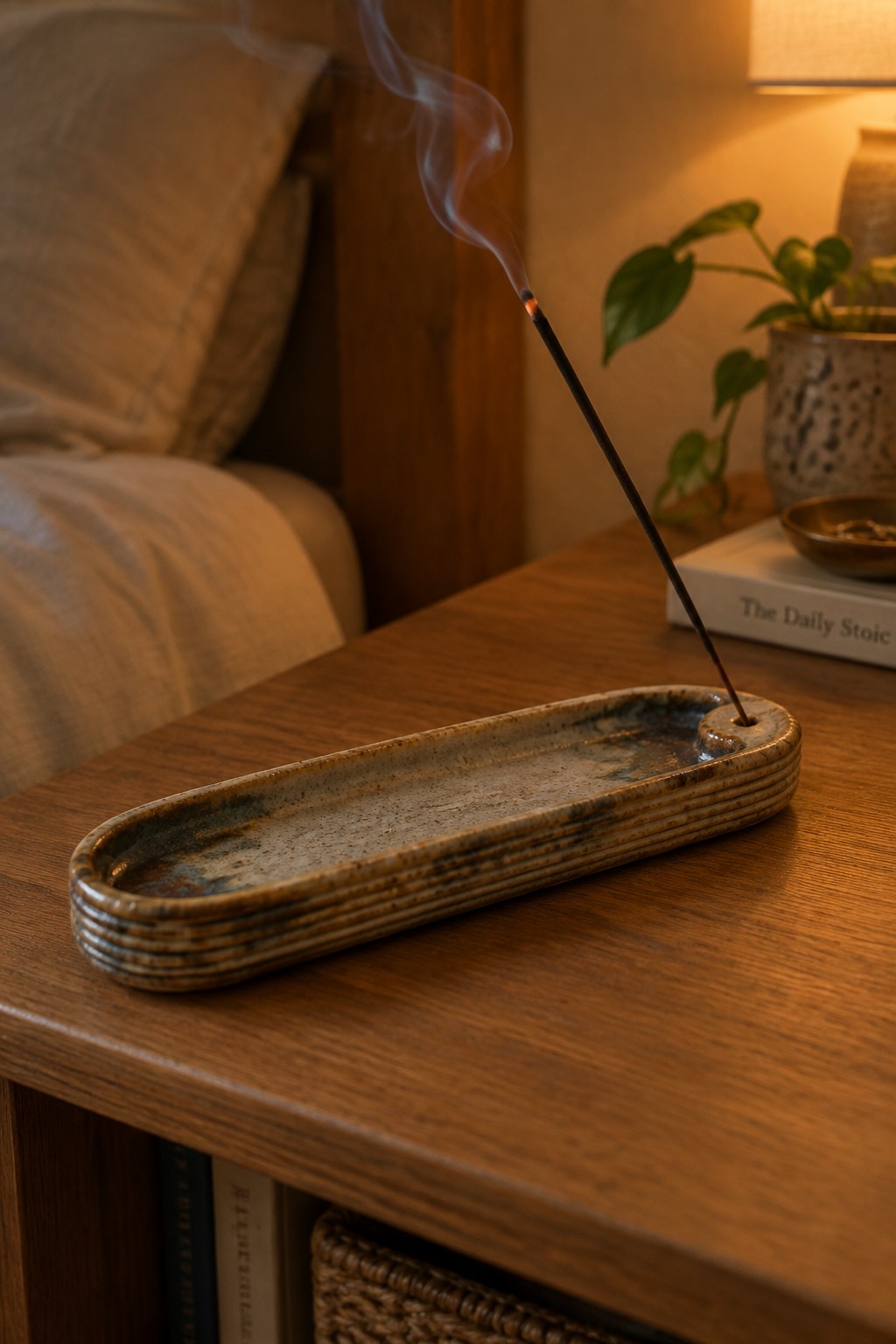 Burning incense stick in a speckled ceramic holder on wooden table, smoke rising.