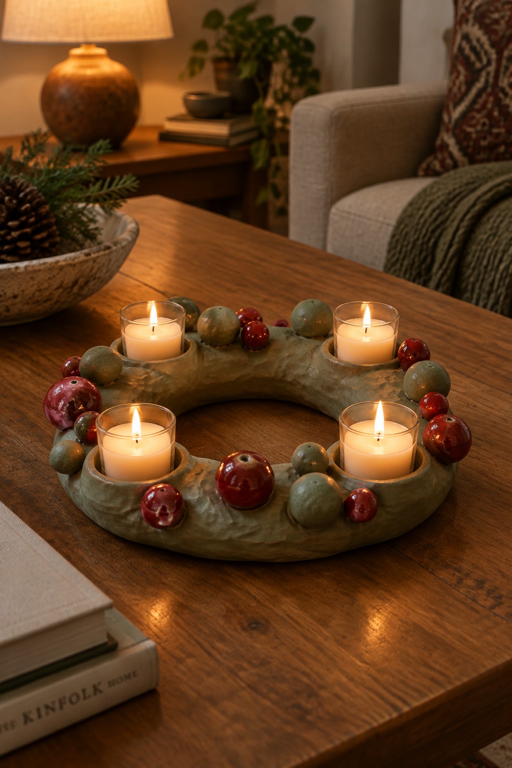 Four lit candles in green ceramic wreath with red and green berries on wooden table