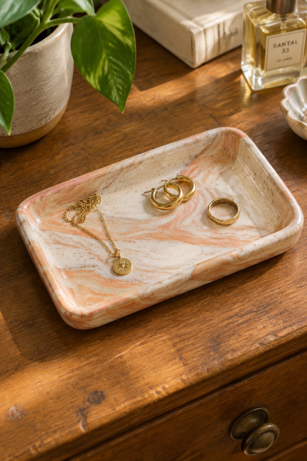 Marble tray with gold sun necklace, hoop earrings, and ring on wooden dresser