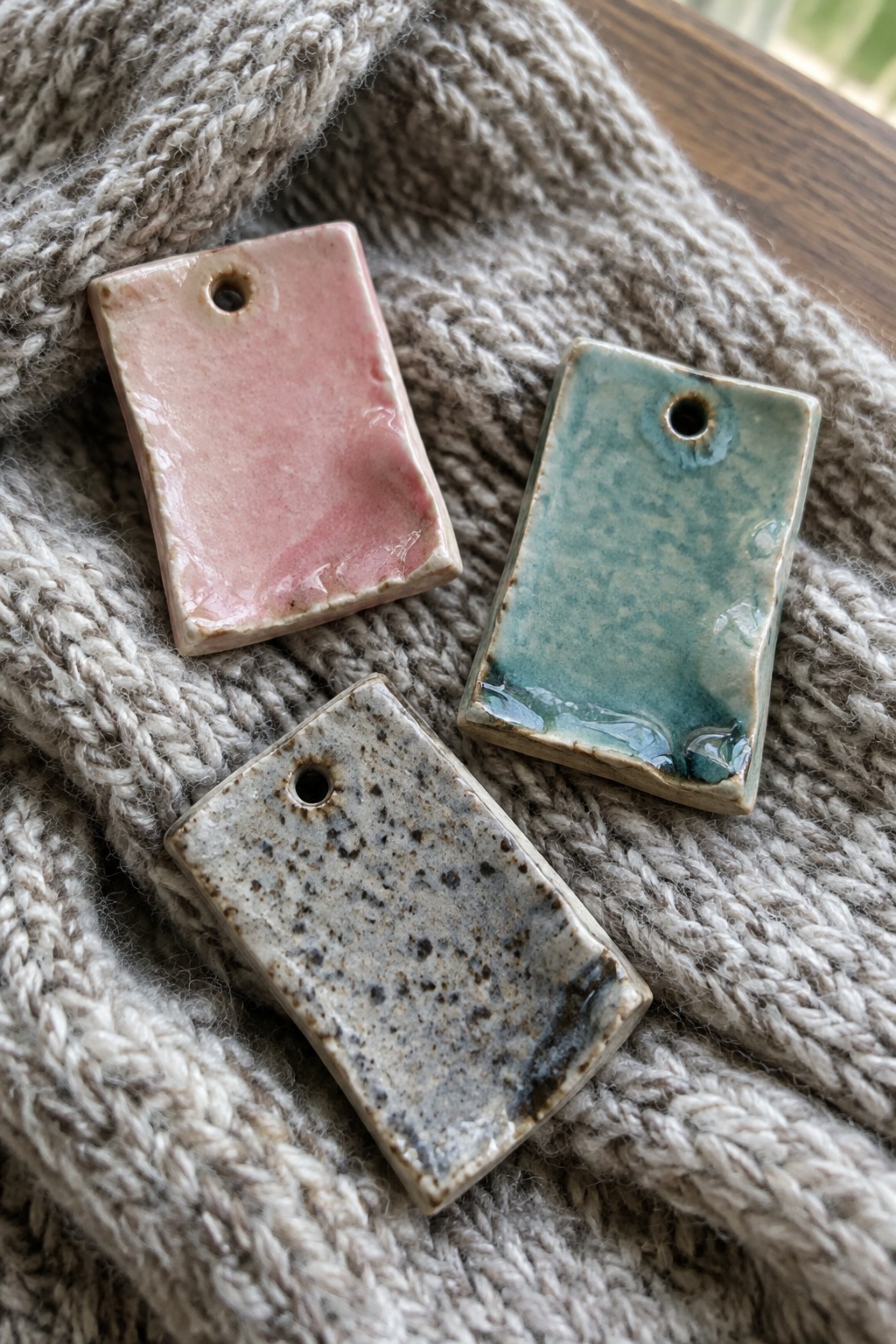Three ceramic pendants in pink, teal, and speckled glaze on knitted sweater.