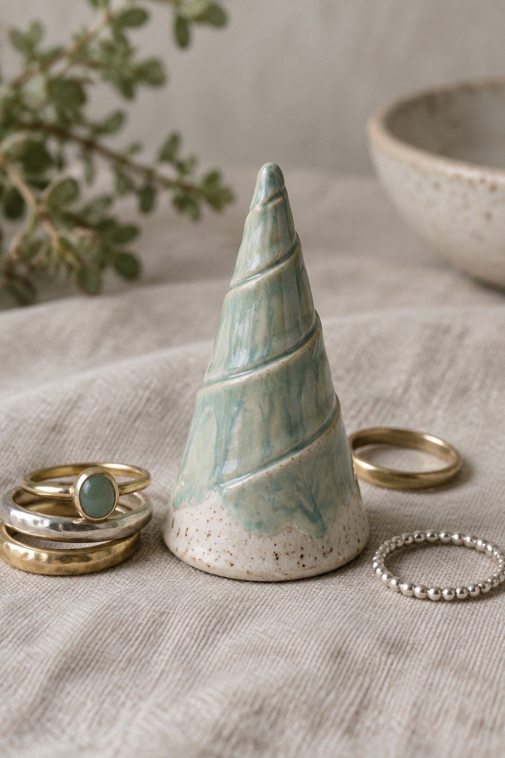 Ceramic turquoise spiral cone ring holder with gold and silver rings on linen