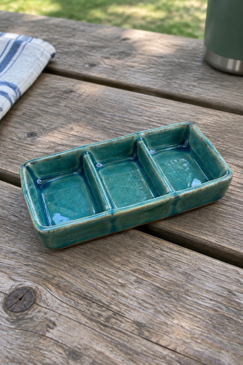 Teal ceramic divided tray on wooden picnic table beside striped cloth