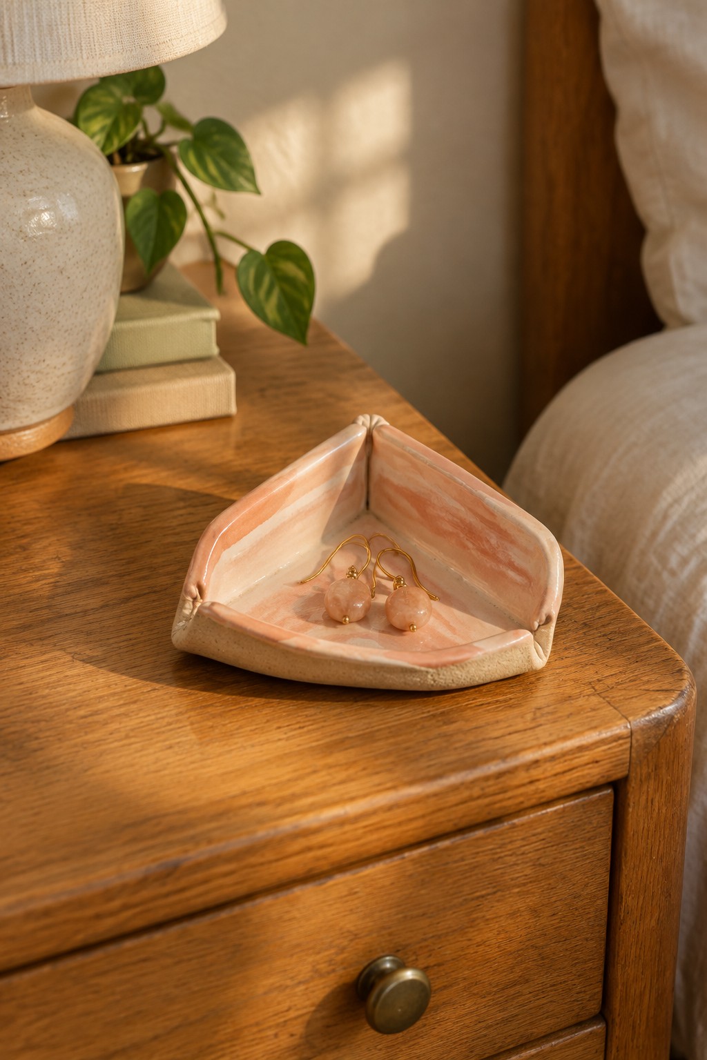 Pink marbled ceramic tray with rose quartz earrings on wooden nightstand