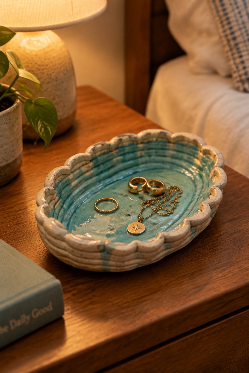 Turquoise scalloped ceramic dish holding gold rings and star pendant necklace on wooden nightstand.