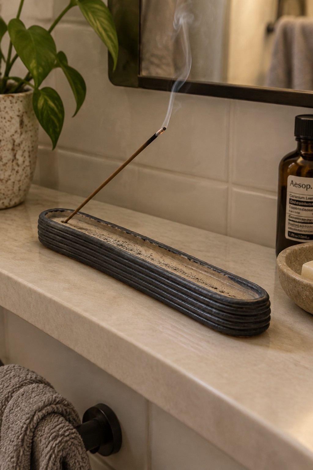 Burning incense stick in dark layered holder on marble bathroom counter with plant