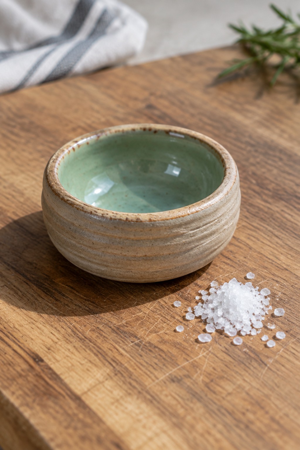 Ceramic bowl with green interior beside coarse salt on wooden board